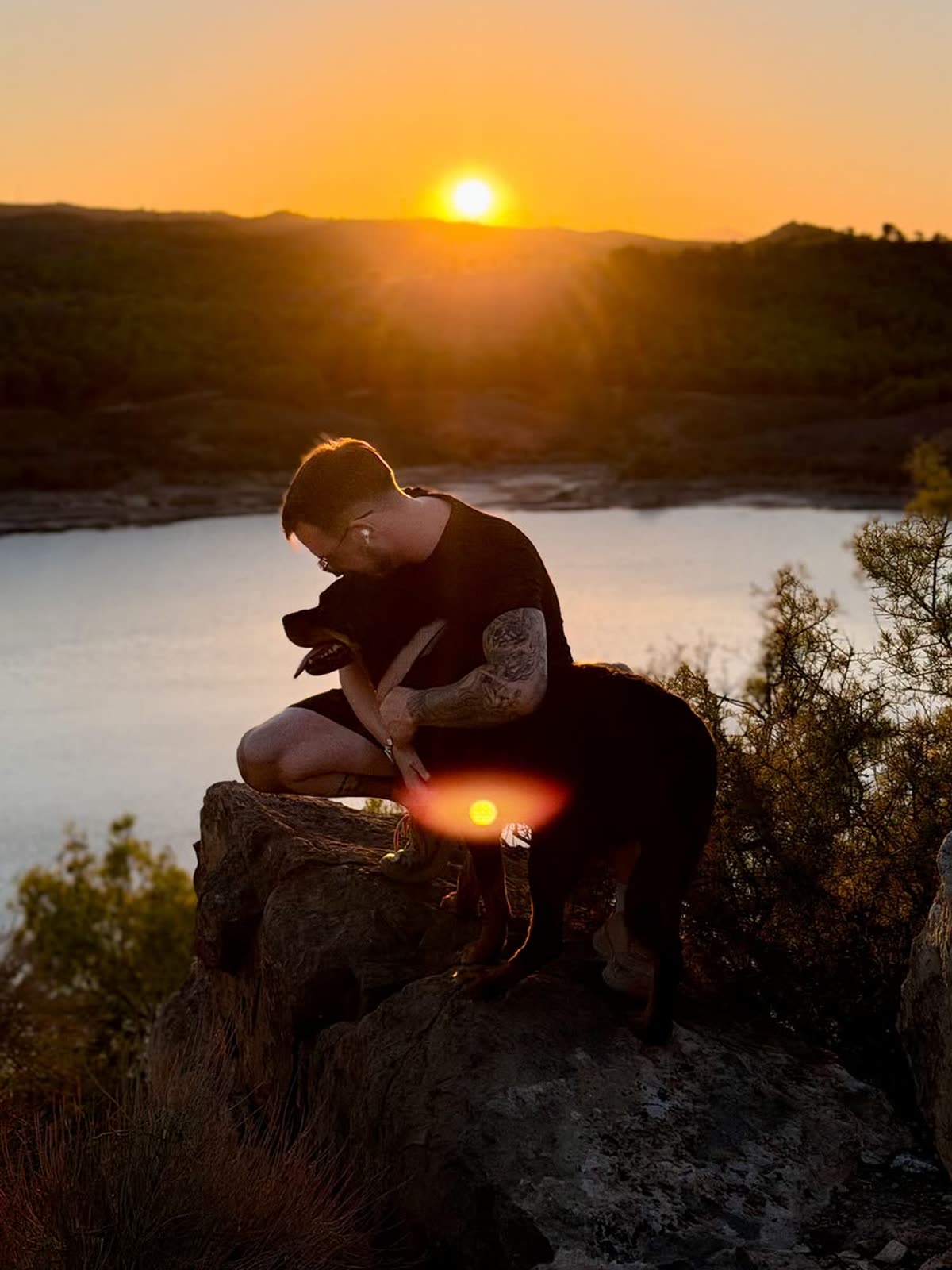 Daniel García con Maya, su rottweiler, al atardecer sobre una roca frente a un embalse en Murcia